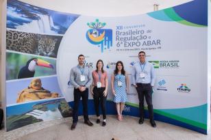 Integrantes da Diretoria de Normas e Regulamentação Ricardo Marcassa Ribeiro da Silva, Marina Beatriz Fantin; a assessora técnica Amanda Vanzella Gonçalvez, da Diretoria da Presidência e o diretor Bráulio Cesco Fleury em frente ao banner do evento.