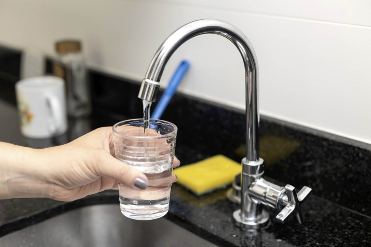 Mão segurando copo e torneira aberta